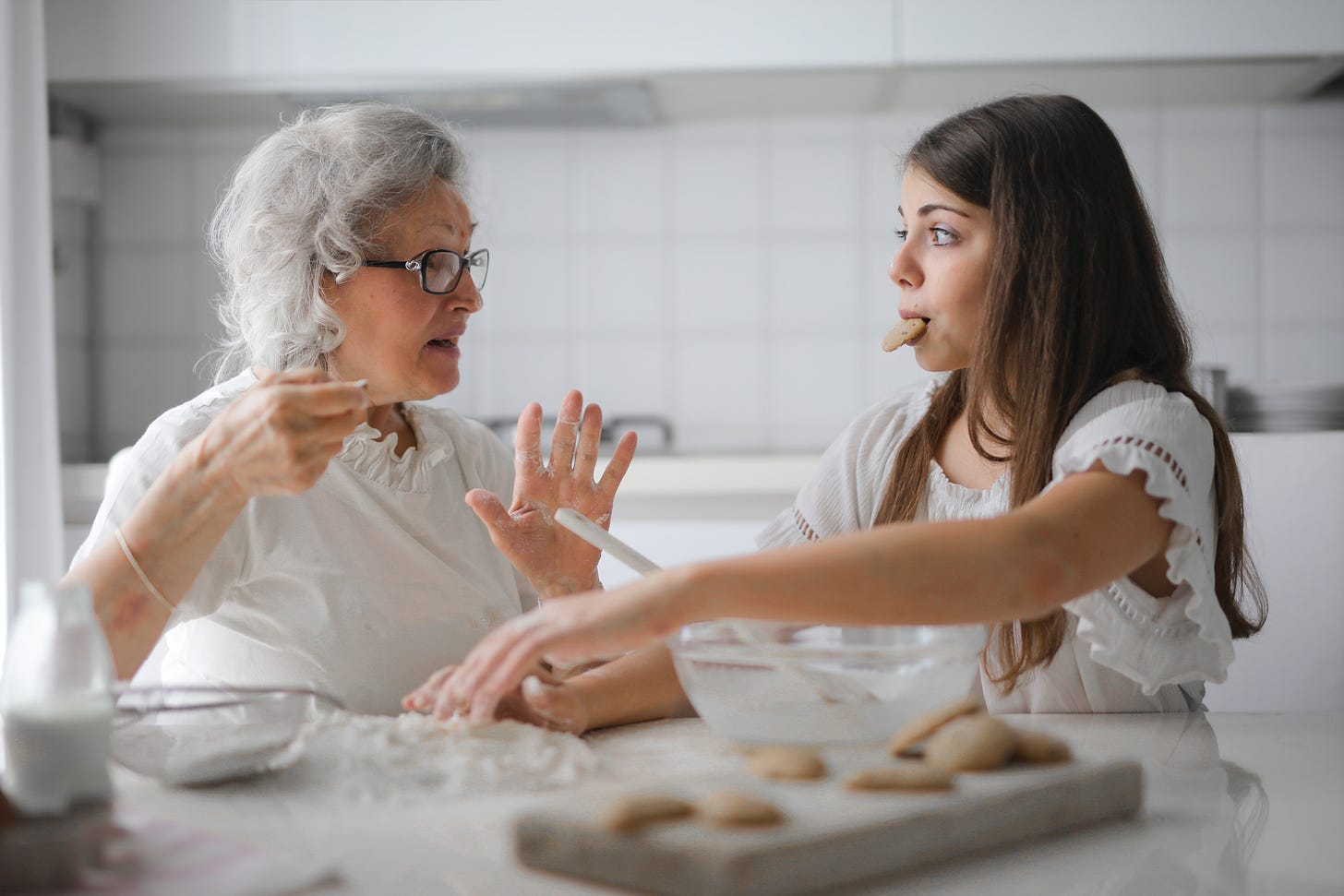 A grandma talking to a young girl while they bake cookies