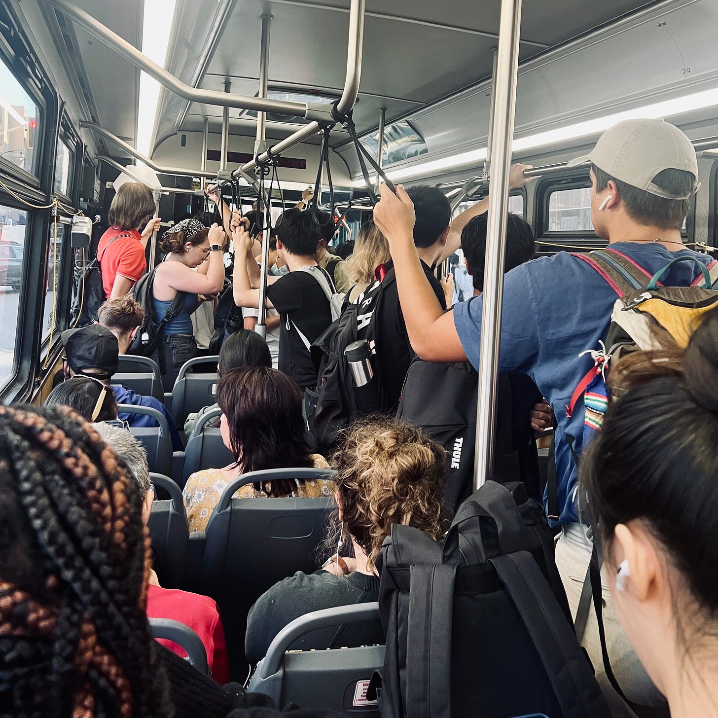 A crowded bus, people are standing up and there is no room to sit.
