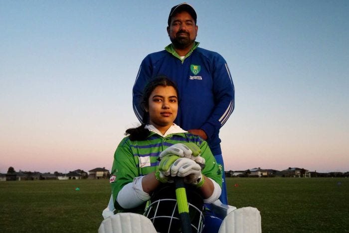 Jamal Mohammed stands behind his daughter, who is dressed in a cricket jumper holding a bat.