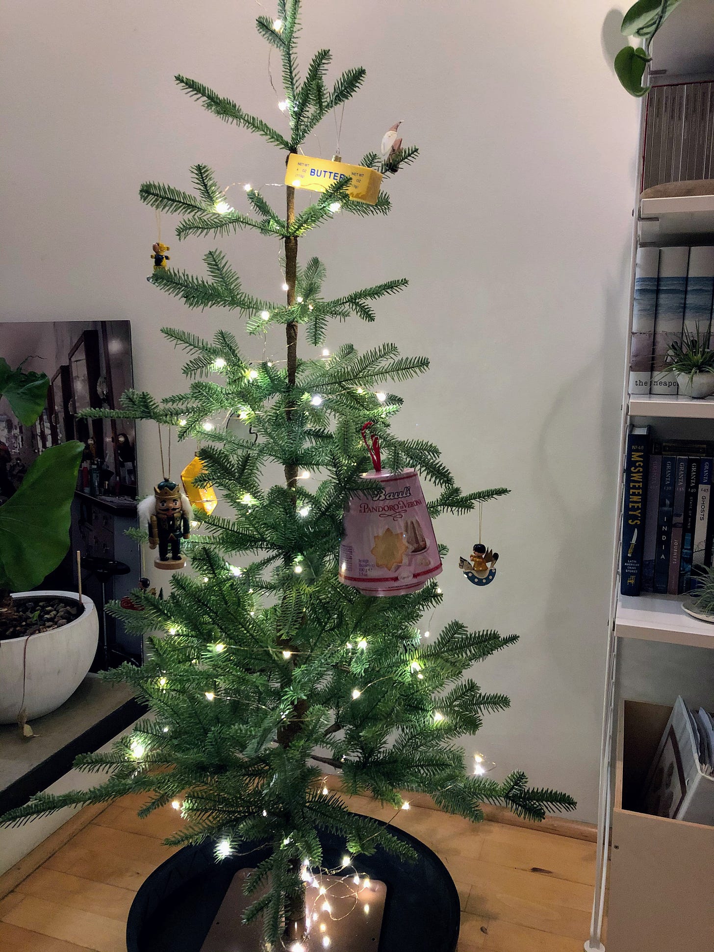 A small decorated Christmas tree with a small box of pandoro hanging on a branch.