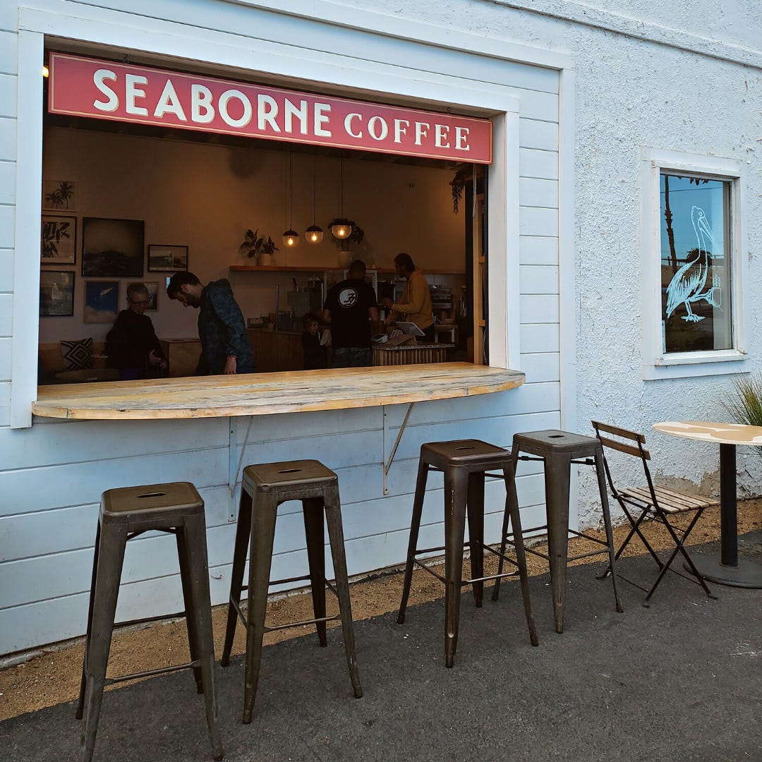 A walk up window to a coffee shop. The Seaborne Coffee sign hangs above and stools are lined up under the window sill for customers to sit while drinking coffee.