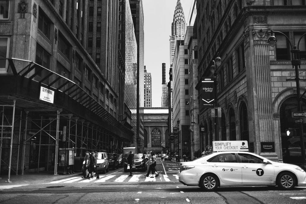 grayscale photography of sedan beside pedestrian