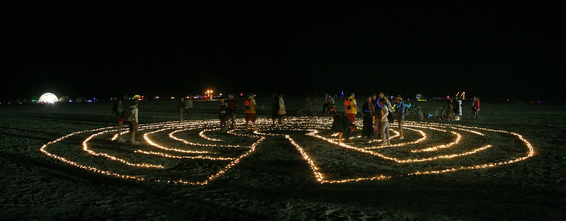 A photo of people walking through a labyrinth at night. The labyrinth seems to be lit by candles. A photo of people walking through a labyrinth at night. The labyrinth seems to be lit by candles.