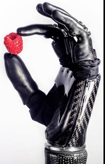Bionic hand holding a raspberry between its thumb and index finger.