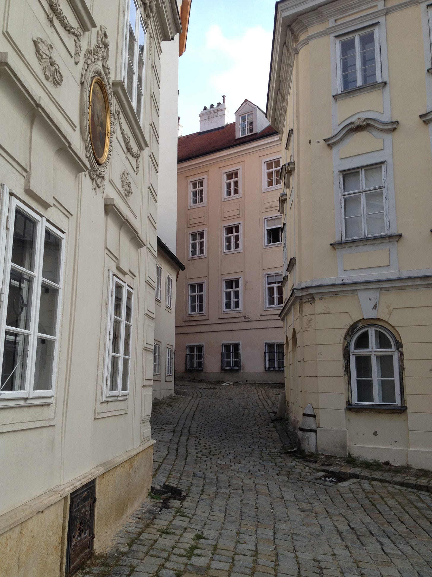 a quiet, empty, street, with old buildings close together and cobblestone pavers in a European city