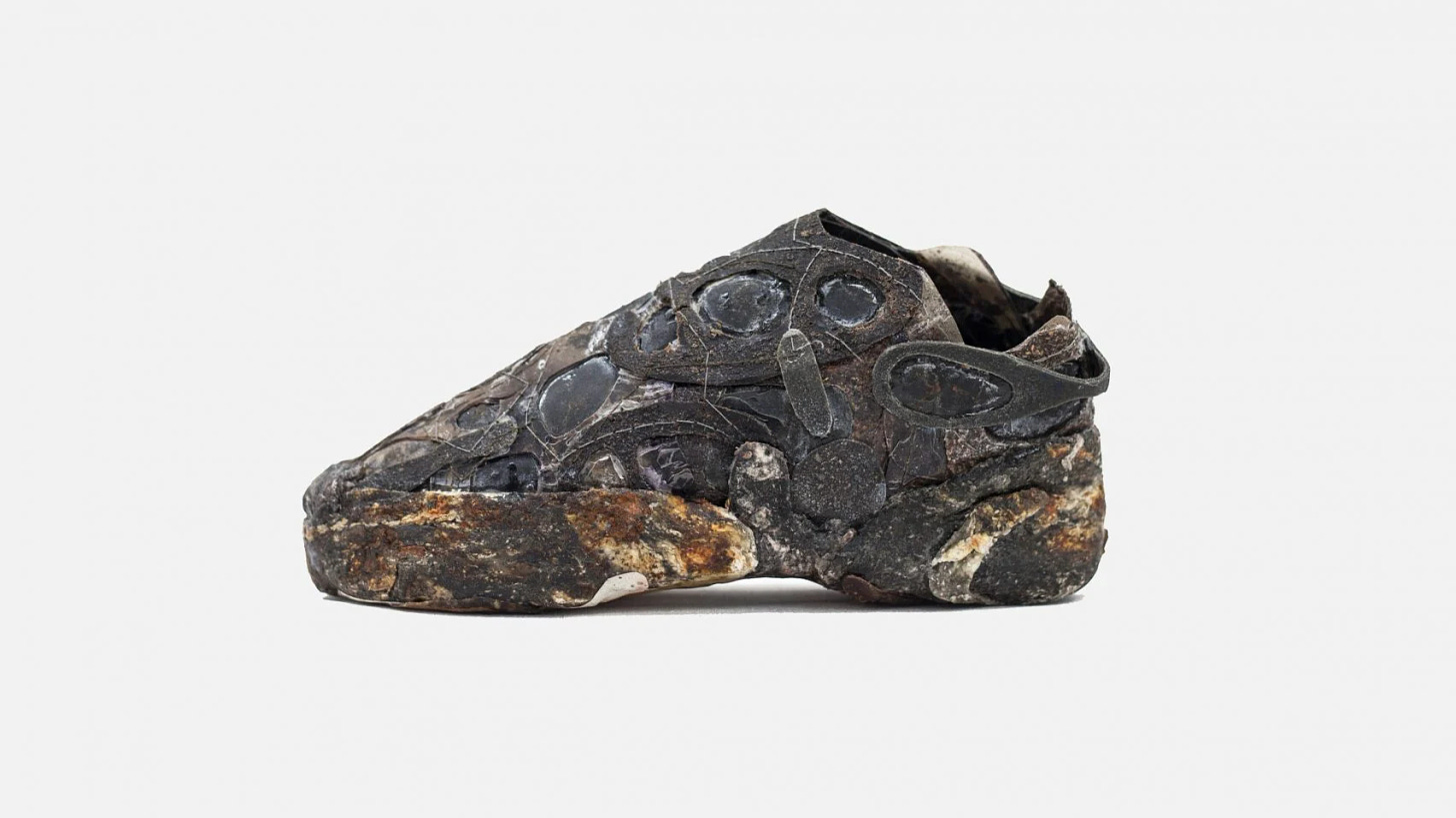 La scarpa realizzata in biomateriali, si mostra con un aspetto scuro e organico, quasi come se fosse passata in una pozza di fango.