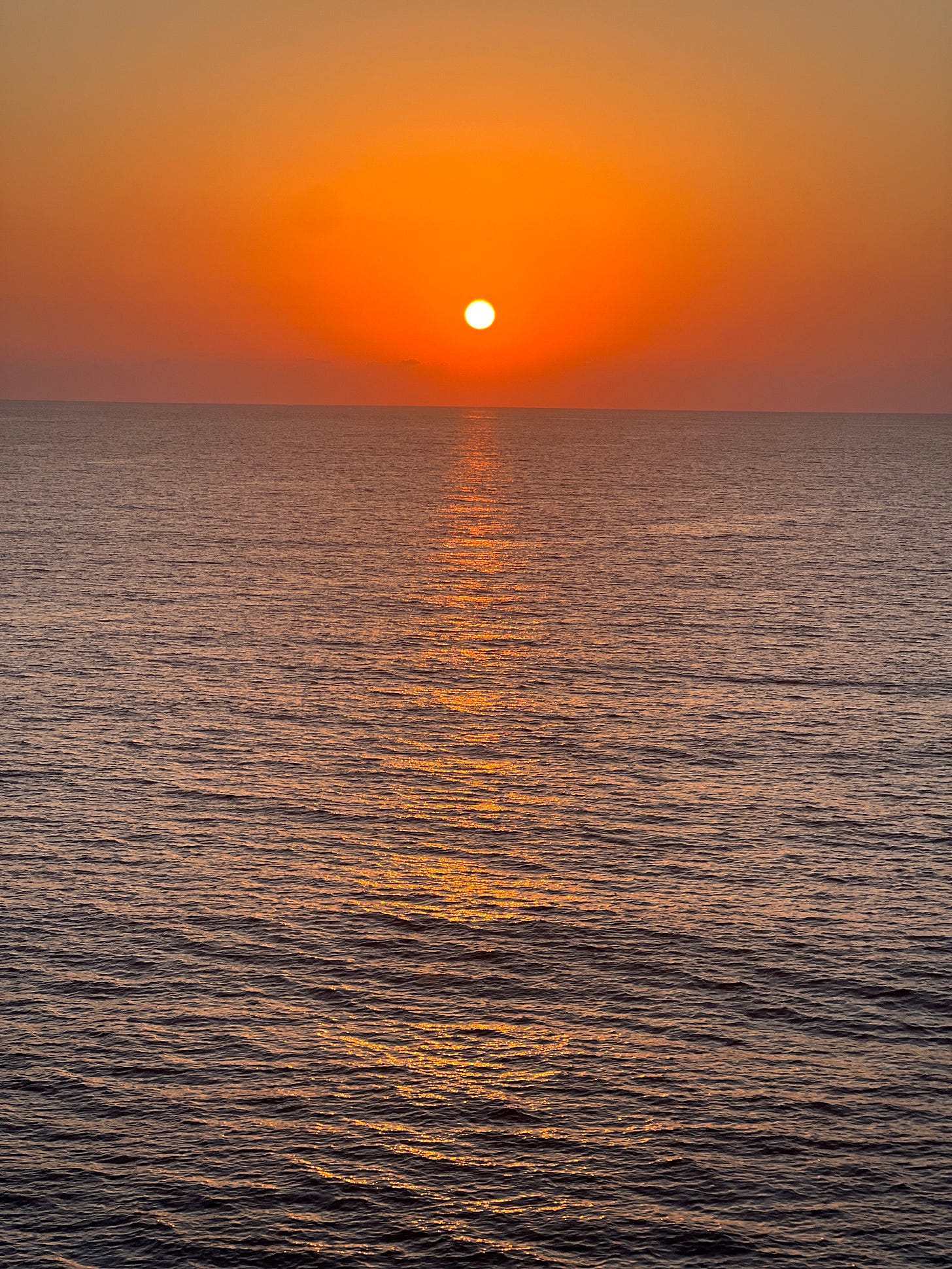 A sunset on the sea, with a beam of bright orange stretching across the ocean