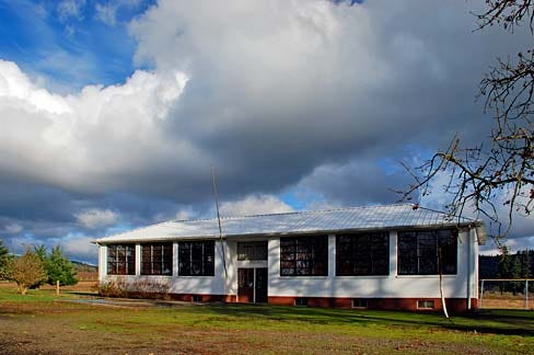 A two-room school building stands beneath a blue sky with clouds. 