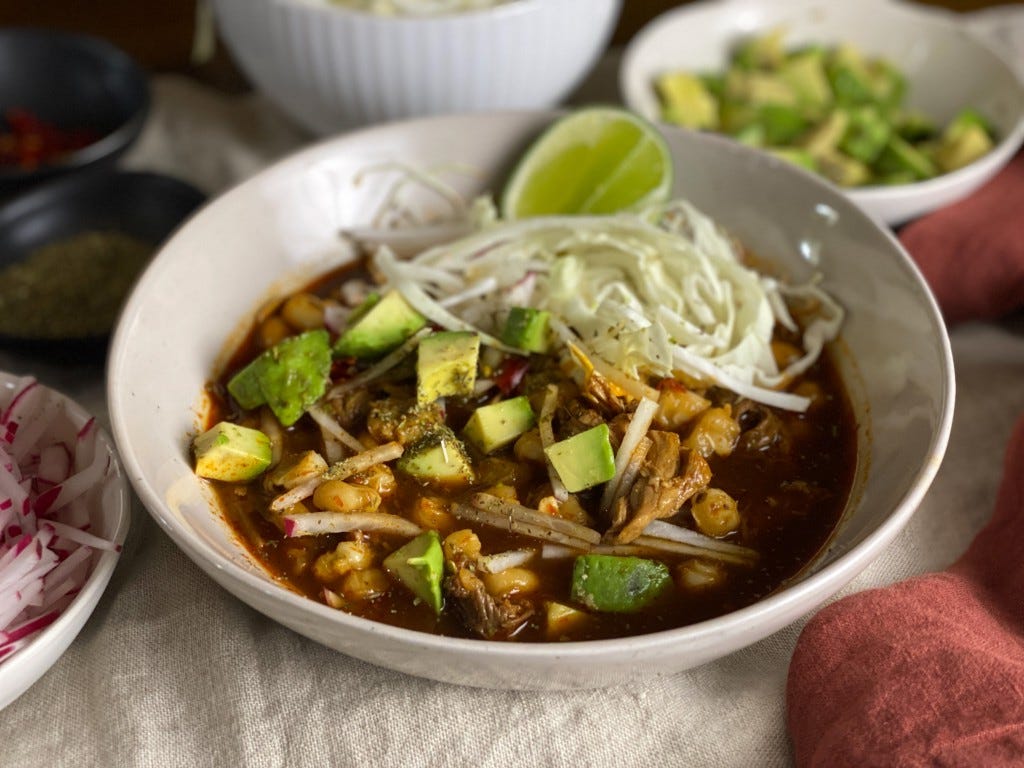 Pozole rojo garnished with avocado, onion, radishes, cabbage and a lime wedge