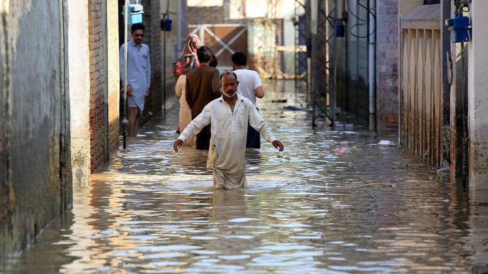 Image shows man wading through flooded street
