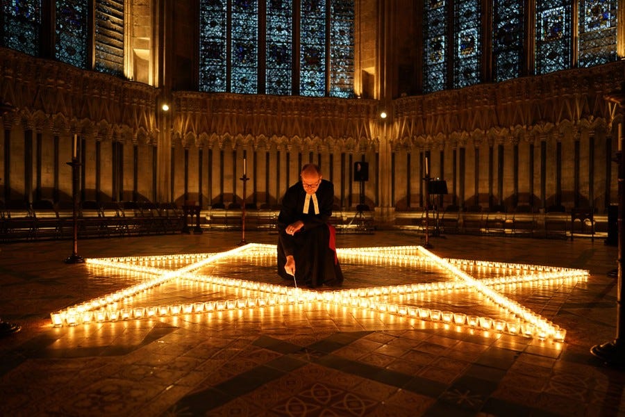 A clergyman kneels on a cathedral floor among hundreds of lit candles arranged in the shape of the Star of David.
