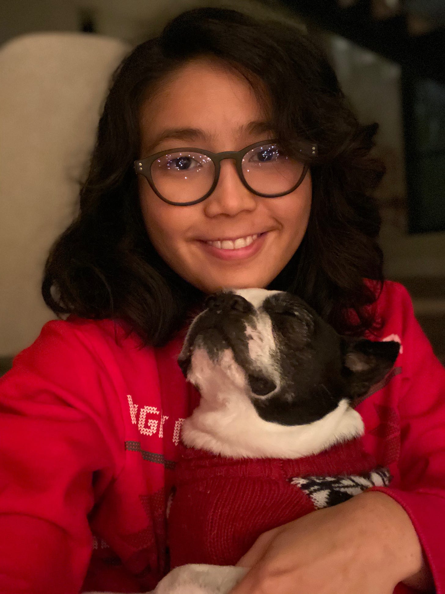 A curly-haired girl with glasses (me!) holds a sleepy black-and-white boston terrier. We're both wearing red sweaters.