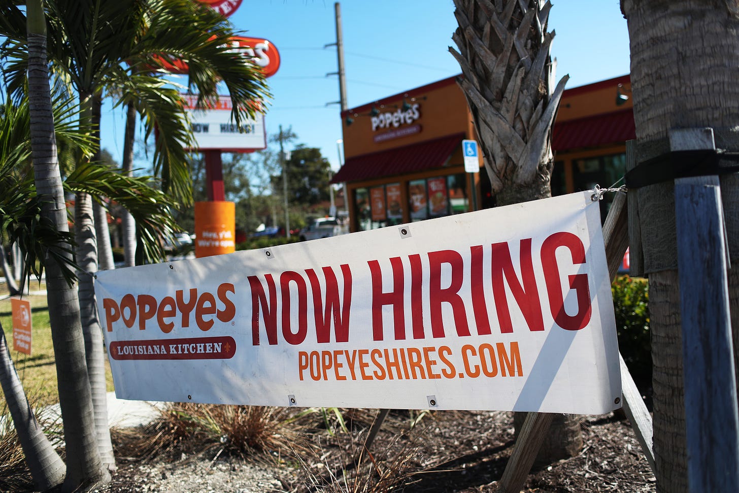 A 'Now Hiring' sign hangs in front of a Popeye's restaurant on February 04, 2021 in Miami, Florida