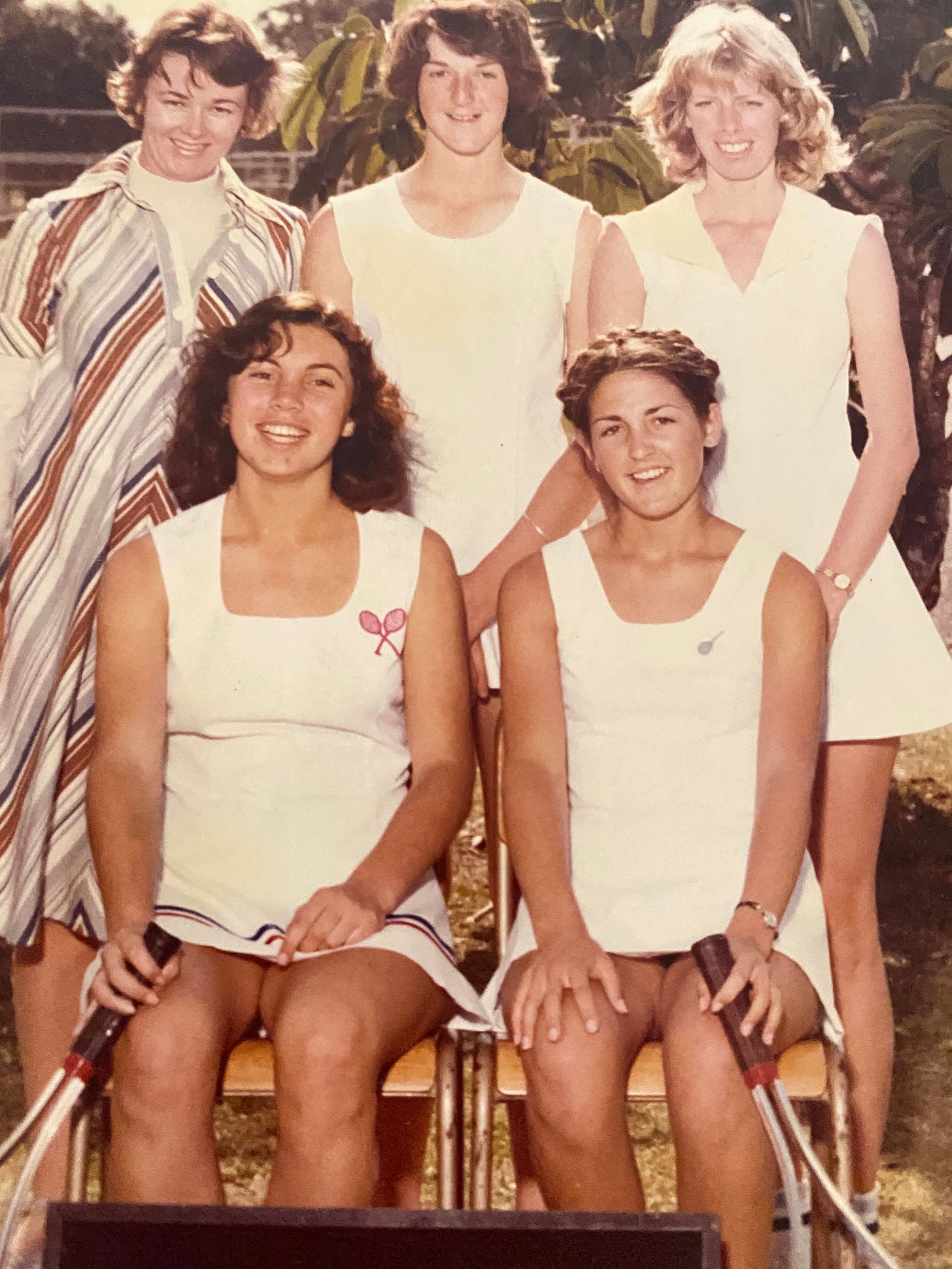 Four young women tennis players and their teacher-coach pose for school photo.