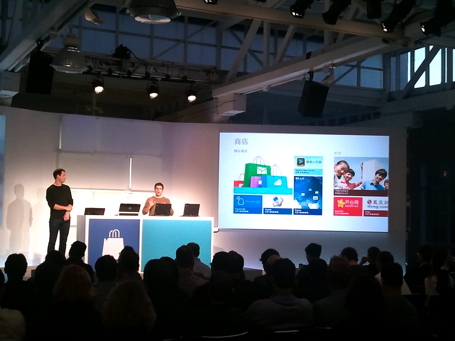 Image of a stage with two presenters and the screen showing the Windows Store in Chinese.