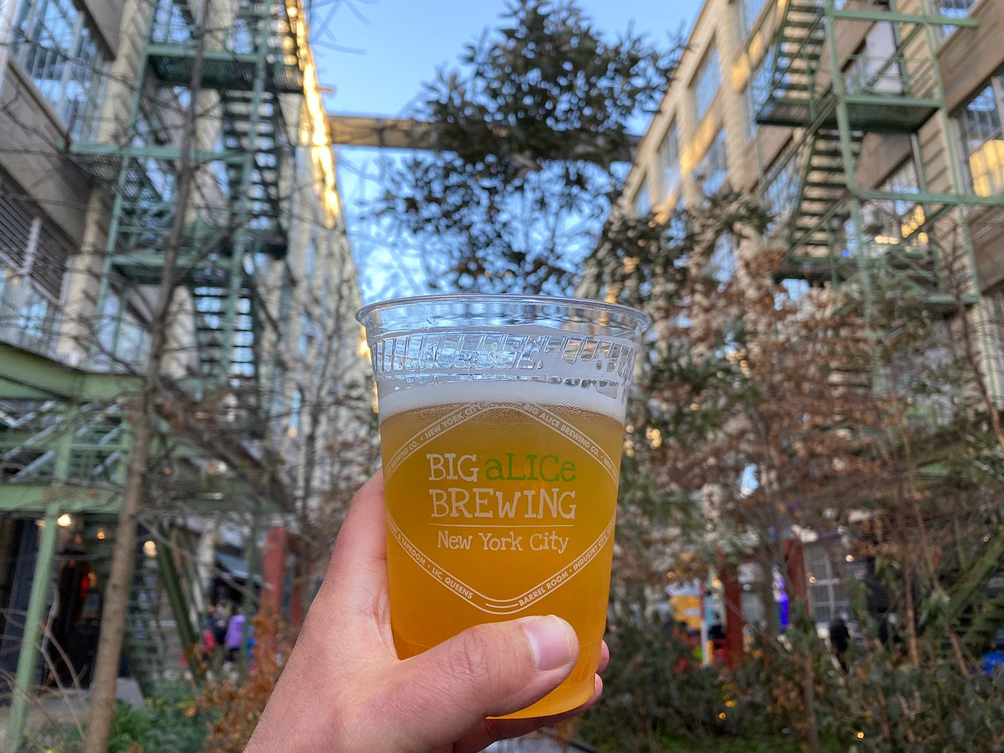 A cup of beer in front of an industrial courtyard with trees