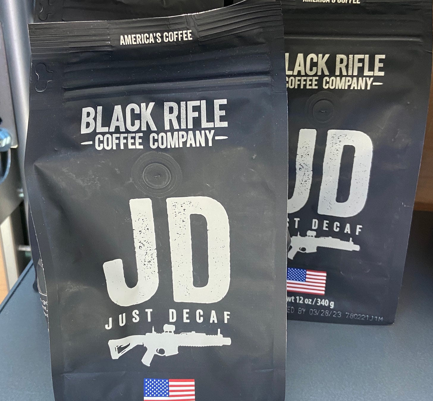 An image of a bag of coffee called "JD Just Decaf" with a graphic of the American flag and an assault rifle.