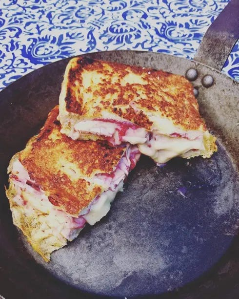 A spun iron pan contains a halved monte cristo sadnwich: teo pieces of bread toasted in the pan with butter and filled with melting cheese, turkey and lingonberry jam 