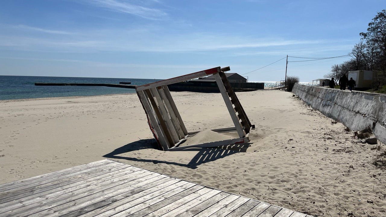 An abandoned beach bed frame (whatever you call these) lies sideways, partially submerged in sand.