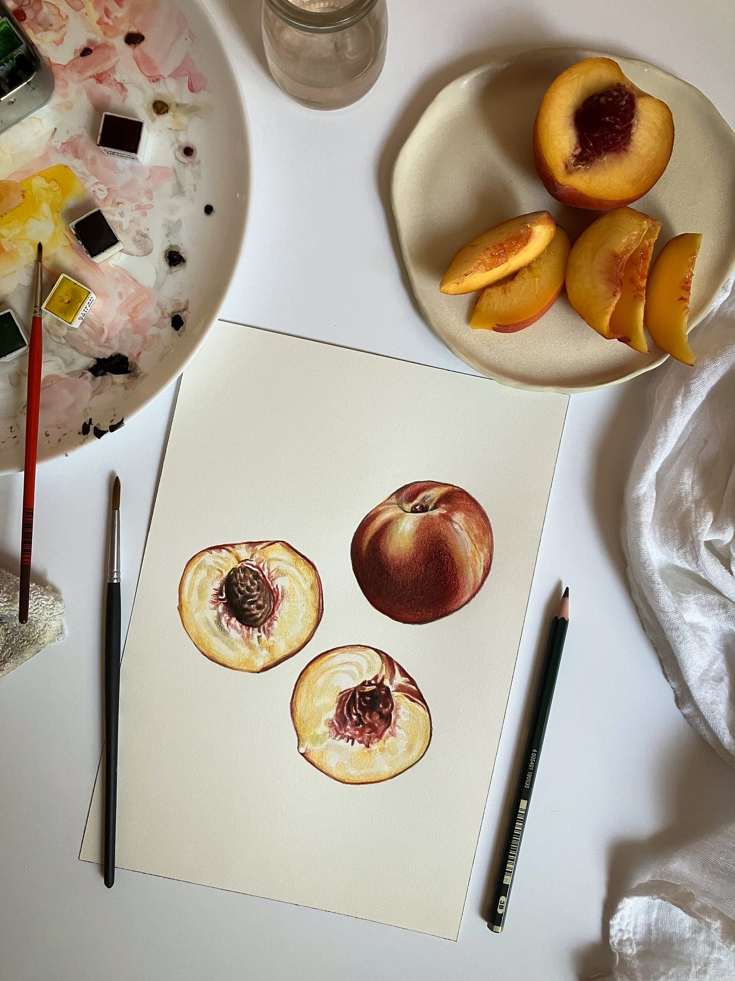 a photo from above of the peach painting being created, with real peach slices on a plate above the painting, and watercolor paints and brushes to the left