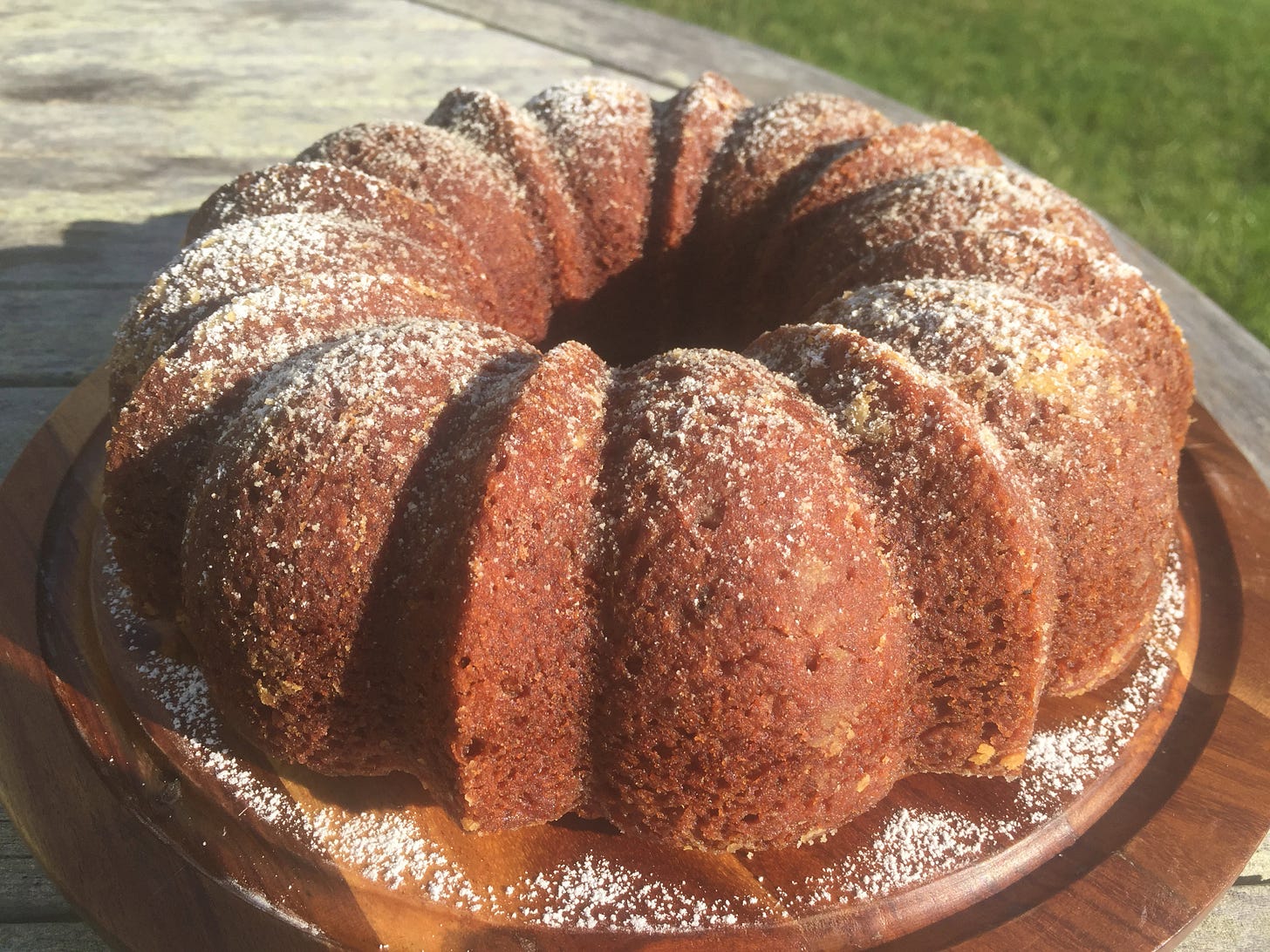 A golden brown ridged bundt cake, dusted with powdered sugar. sits on a platter on an outdoor table.