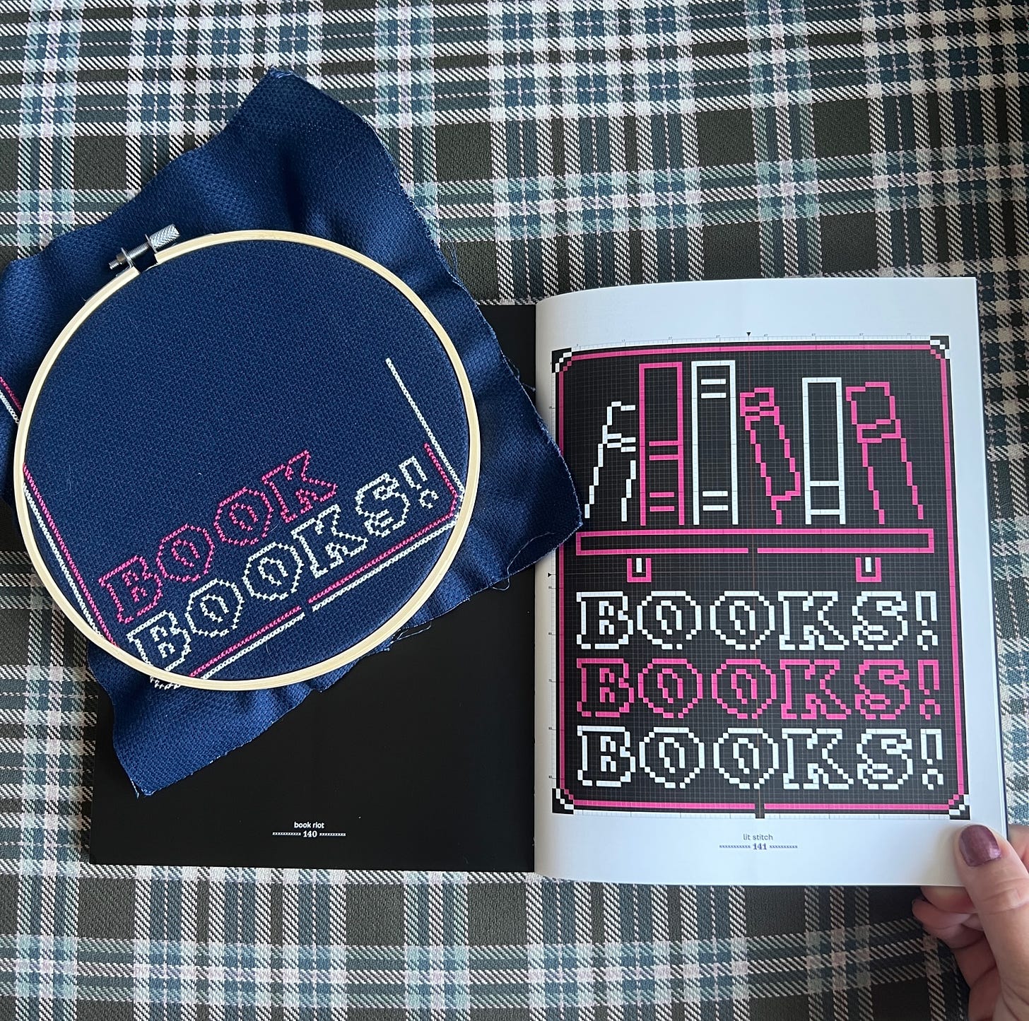 A cross stitch hoop with a partially finished project in it. The pattern repeats Books! Books! Books! in pink and white. 