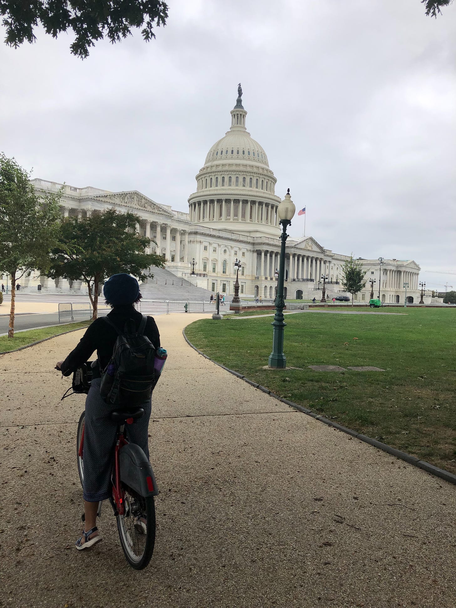 Kristen in the foreground as a shadowy figure on a Capital Bikeeshare bike looking up at the US Capitol on an overcast day