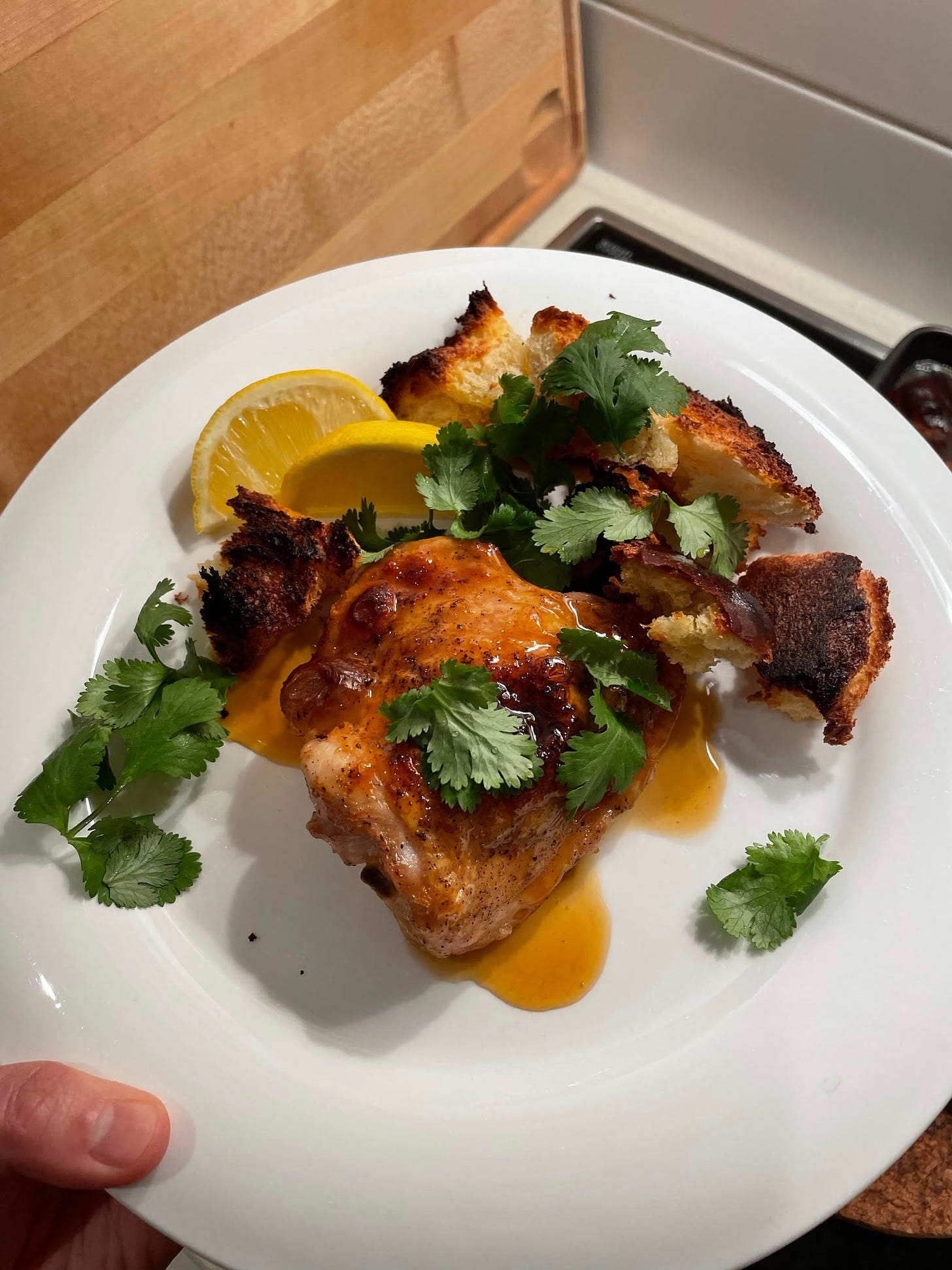 A plate of roast chicken and croutons topped with coriander and served with lemon