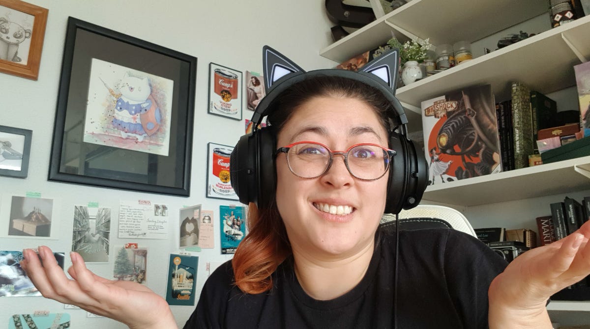 A woman wearing glasses and a black shirt shrugging. She is wearing headphones with cat ears. There are postcards on the left and a bookshelf on the right.