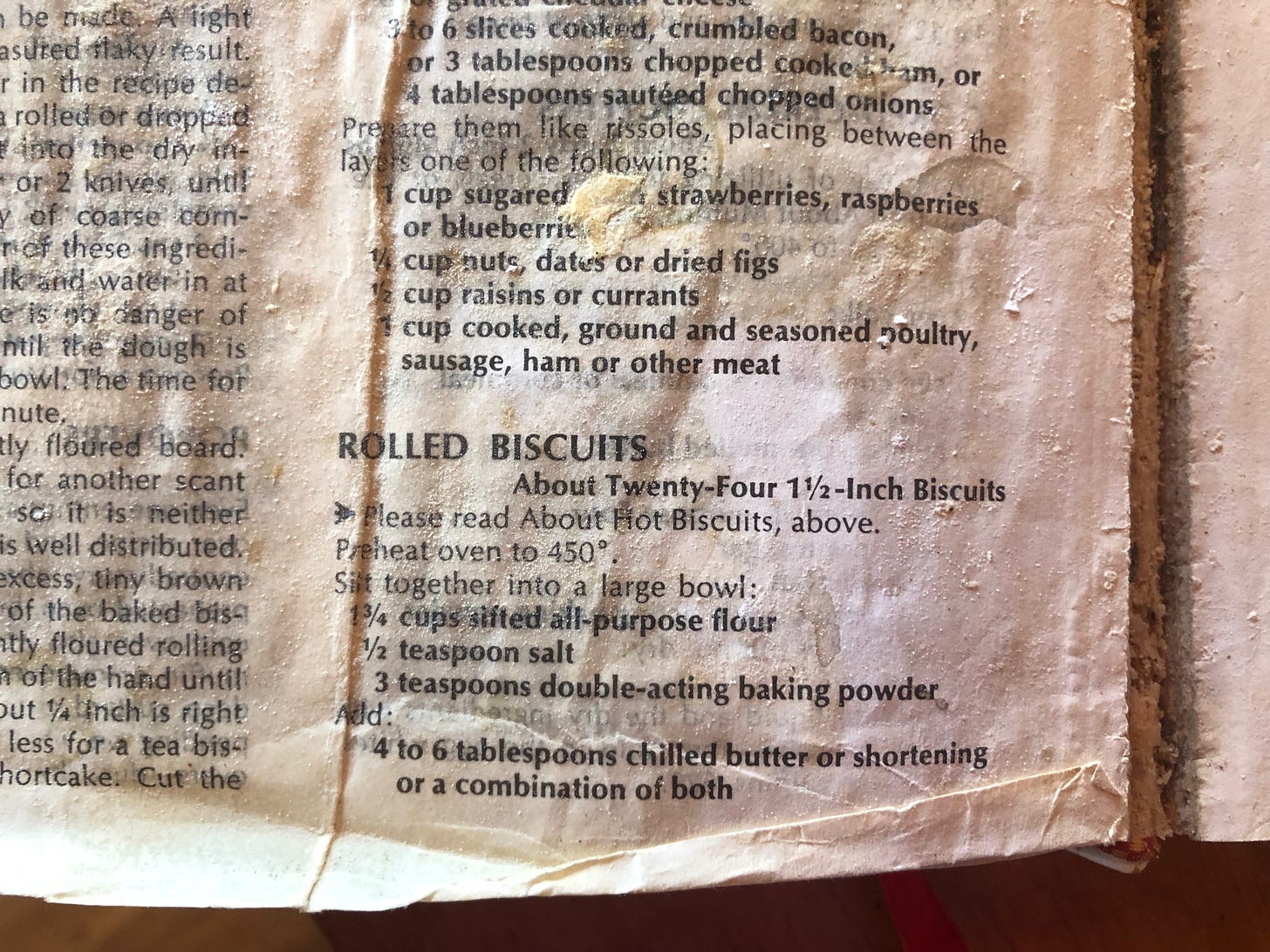 Photo of a page from The Joy of Cooking, showing the recipe for Rolled Biscuits. The page is covered with stains, bits of crusty flour, wrinkles, and tears.