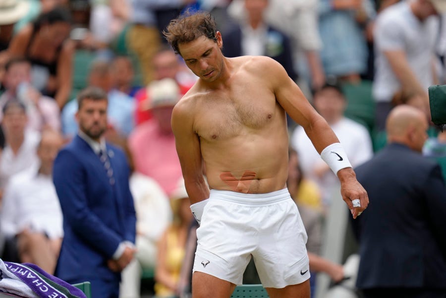 Spain's Rafael Nadal sports tape on his stomach following a medical timeout as he plays Taylor Fritz of the US in a men's singles quarterfinal match on day ten of the Wimbledon tennis championships in London, Wednesday, July 6, 2022.