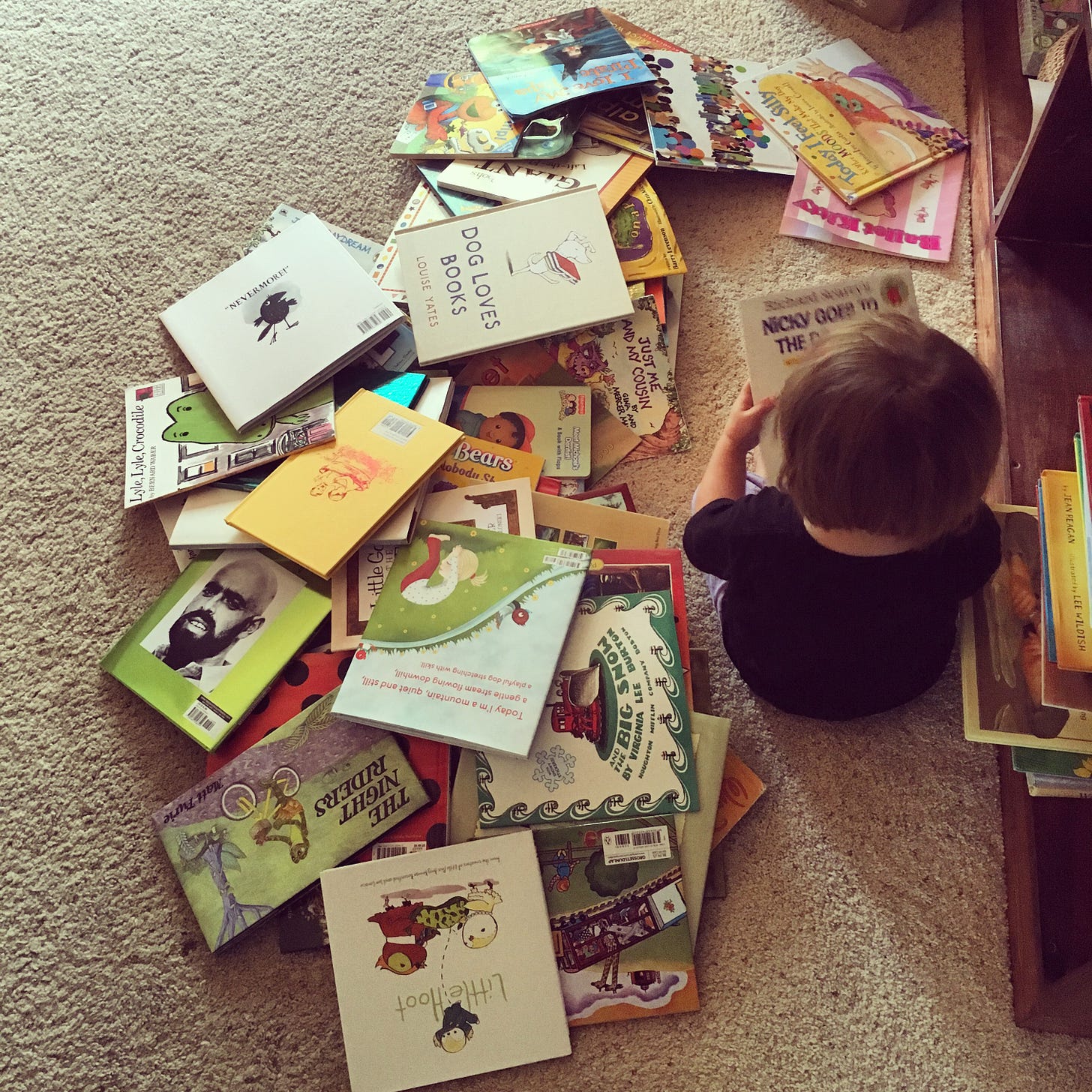 A toddler girl sitting next to a huge pile of picture books