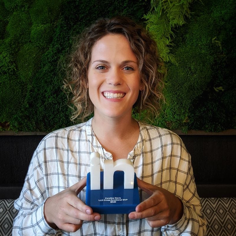 a mid 20s white woman with shoulder length curly hair smiling and holding an award that says LinkedIn cross functional MVP