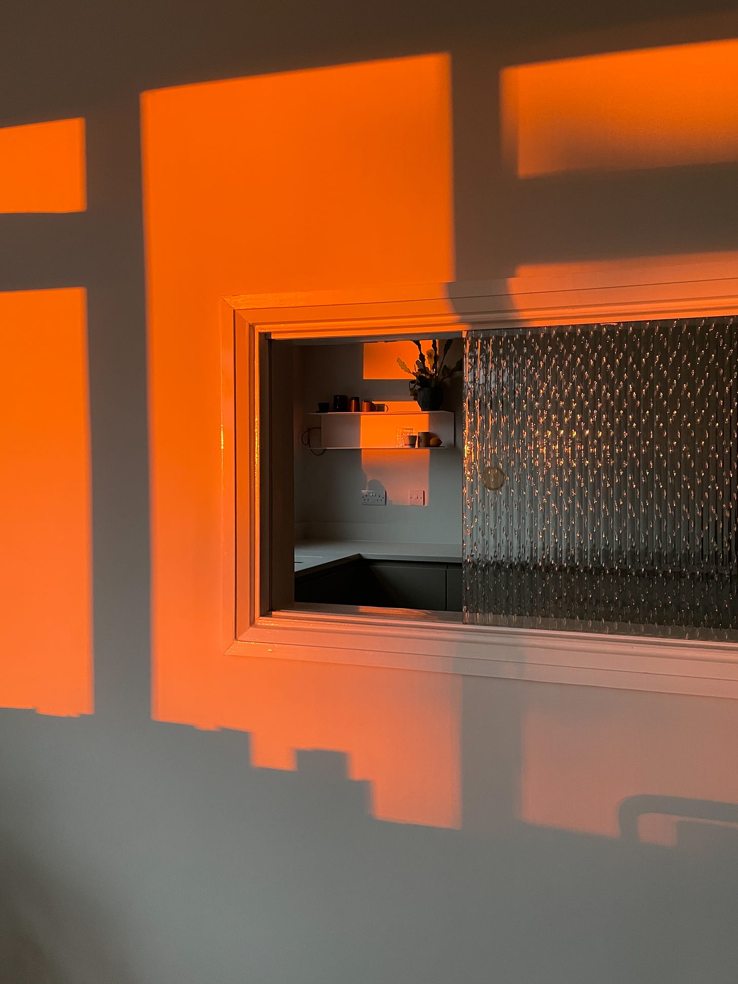 A wall with a window through to another room. The entire scene is lit by the morning sun and is fiery orange.