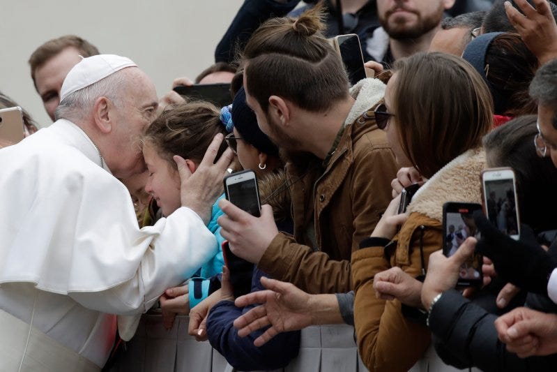 Pope Francis kisses a child in St. Peter's Square at the Vatican before leaving after his weekly general audience, on Feb. 26, 2020.