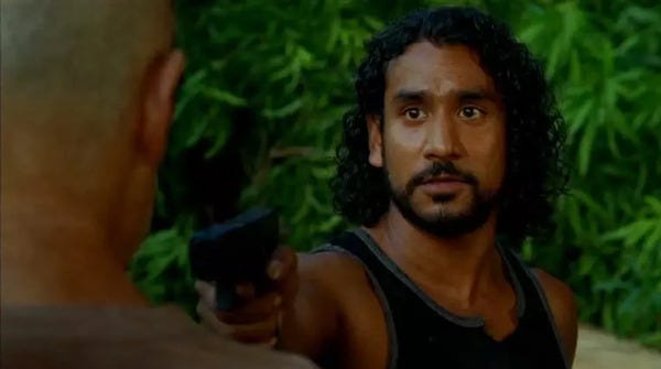 Sayid Jarrah (Naveen Andrews) points a gun at John Locke (Terry O’Quinn), the back of whose head is visible in the extreme left foreground.