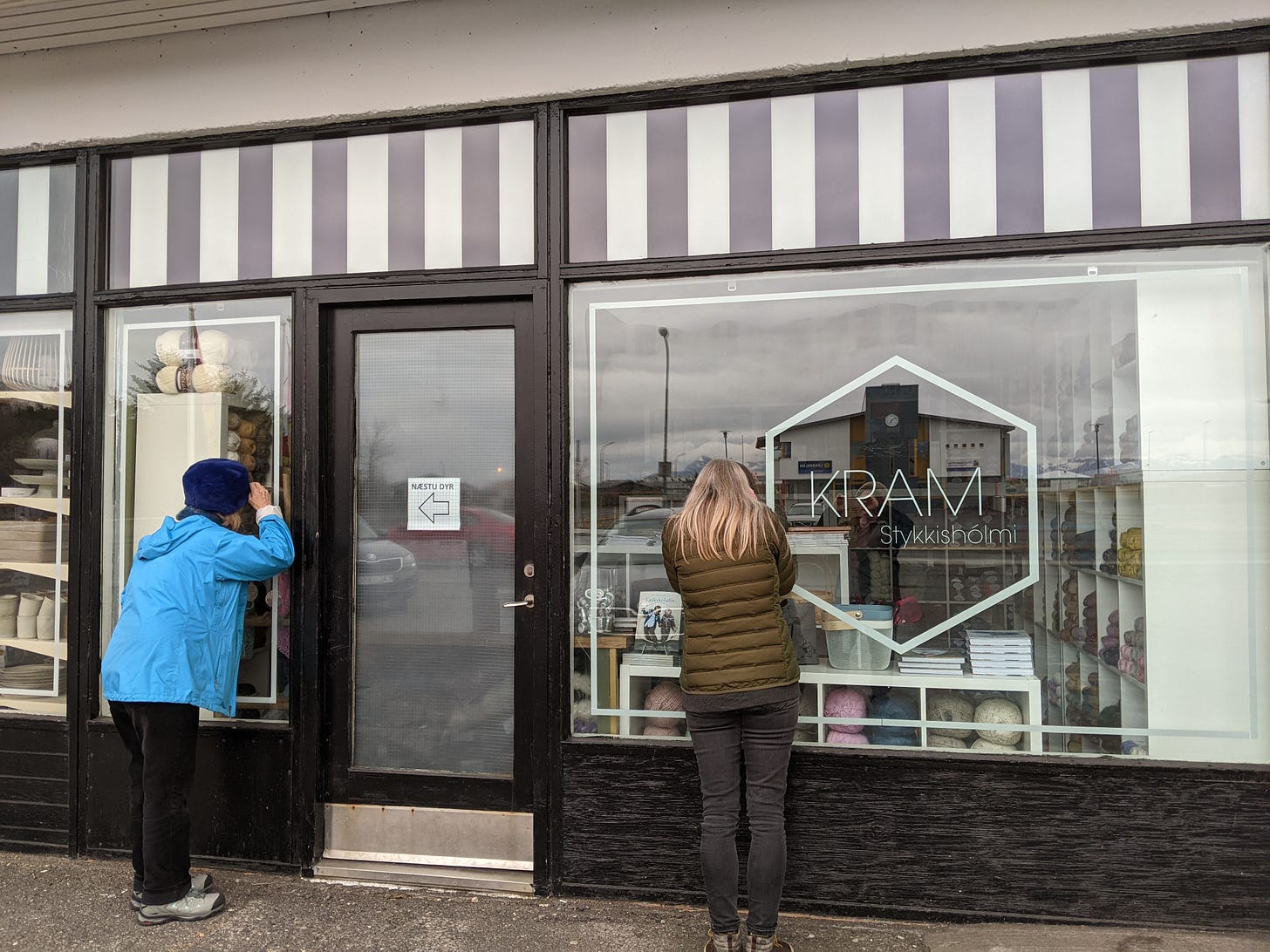 Two women peering through the closed store window of knitting store Kram in Stykkishólmi, Iceland.