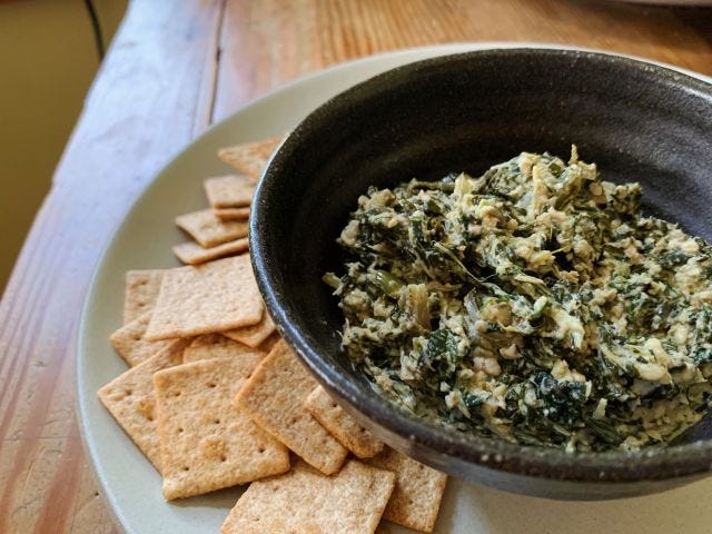 A brown bowl with a white and green spread in the middle and crackers on the side