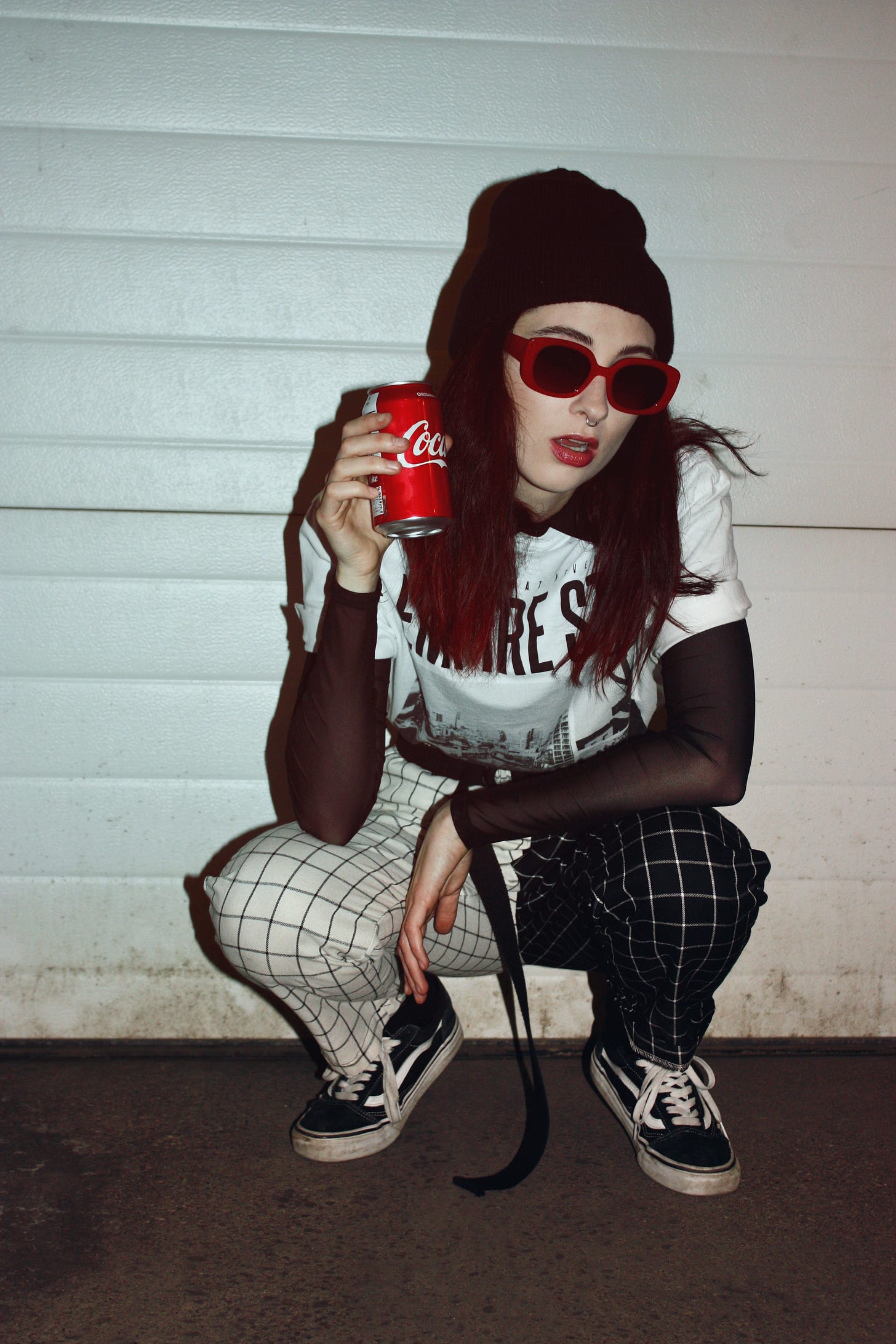 A young woman squats off center holding up a Coke can.