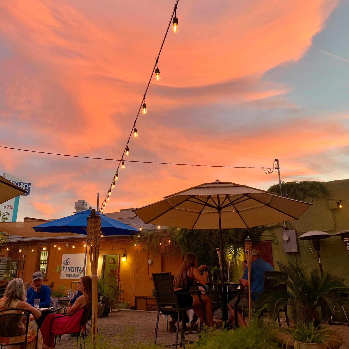 The red-orange sunset over the outdoor seating area of a Tucson restaurant illuminated with string lights.