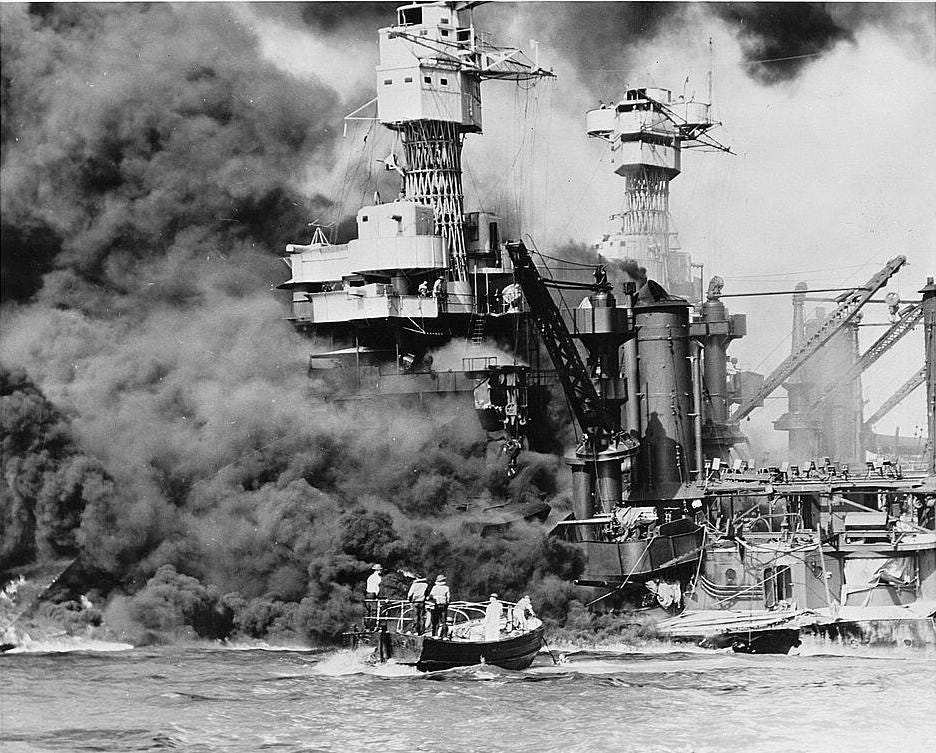 Wikimedia description: "A small boat rescues a seaman from the 31,800 ton USS West Virginia burning in the foreground. Smoke rolling out amidships shows where the most extensive damage occurred. Note the two men in the superstructure."