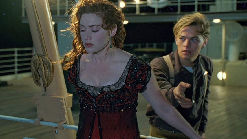 Rose holding onto the railing of the ship while Jack offers a hand to pull her back