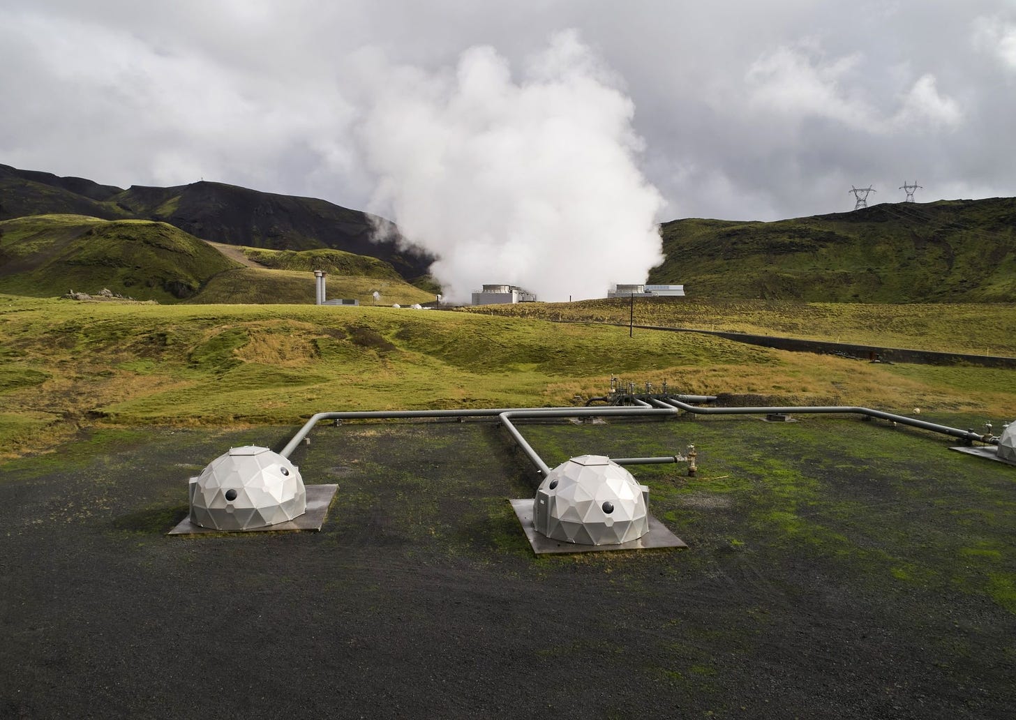 A picture looking across the Orca direct-air capture plant in Iceland, showing two of the domes and the pipework supplying them