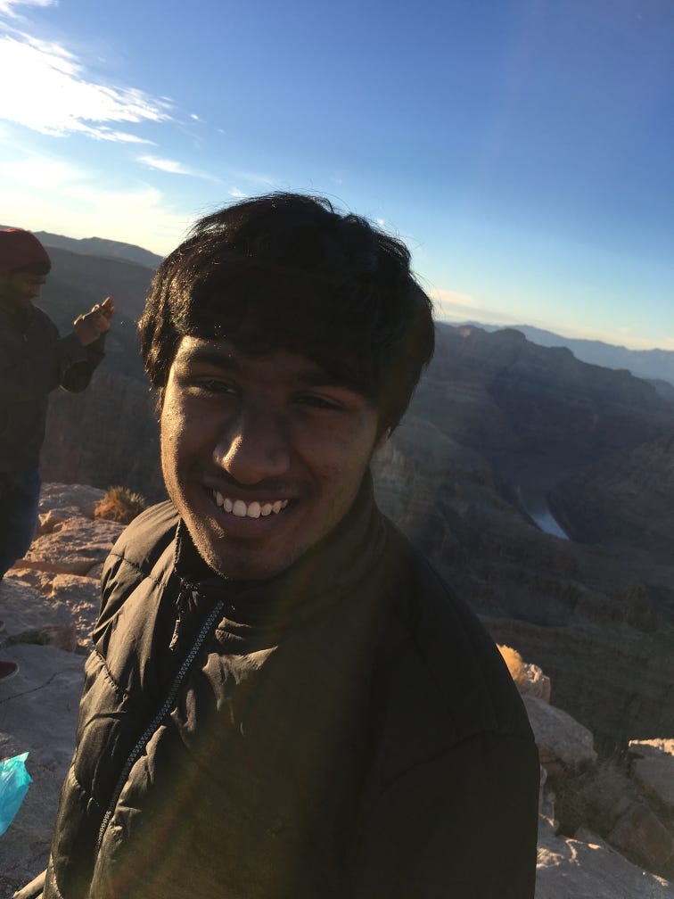 Kani Krishnan stands, smiling, in a dark green jacket before a breathtaking landscape of canyons.