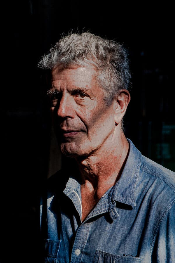 A moody-looking man with graying hair and a blue-jean shirt stares at the camera with shadows accenting his face.