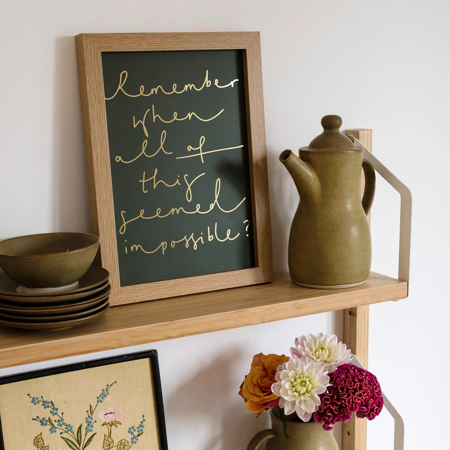 A shelf with a framed print that reads 'Remember when all of this seemed impossible' in handwritten text.