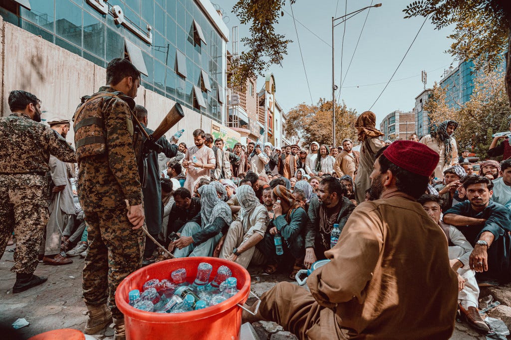 Taliban guards hand out water bottles to Afghans waiting to withdraw cash.