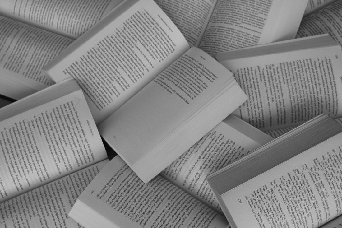 Foto em preto e branco de um monte de livros abertos sobre uma mesa.