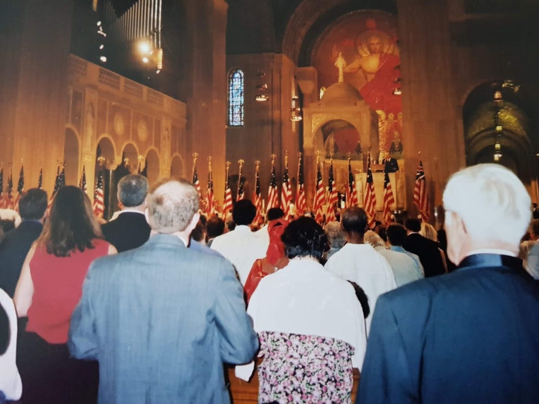 Interiören från en kyrka. Man ser ryggarna av en stor grupp människor och en rad amerikanska flaggor. Längst fram i kyrkan syns en altarmålning av Kristus.