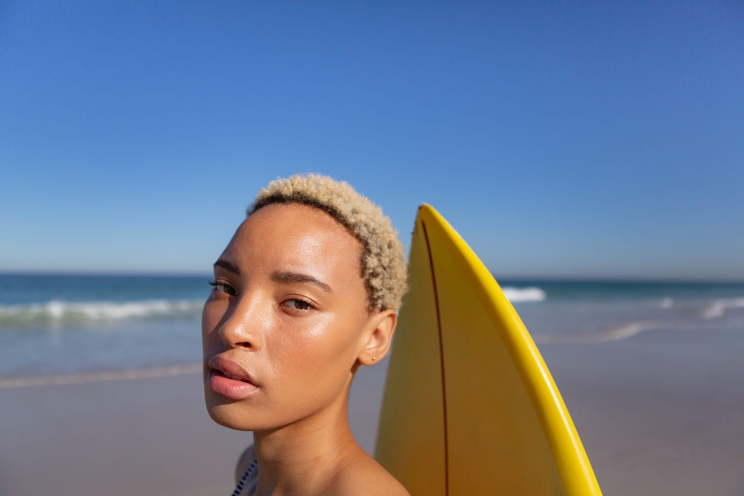 Close-up of beautiful African american woman standing with surfboard on beach in the sunshine.
